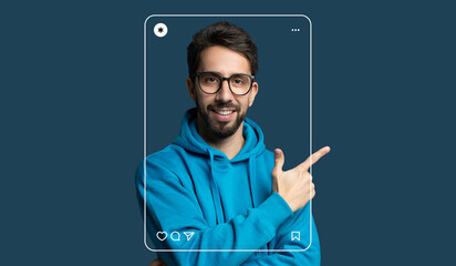 A young man with glasses is smiling and pointing while wearing a blue hoodie. He appears confident...