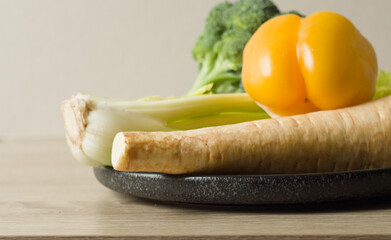 A plate of fresh, raw vegetables: broccoli, yellow bell pepper, celery, and a parsnip