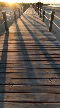 Strolling at sunset along a wooden boardwalk over the beach dunes. Wooden walkways installed to protect the dunes and their flora and fauna, on Riumar beach in Catalonia, Spain. Vertical.