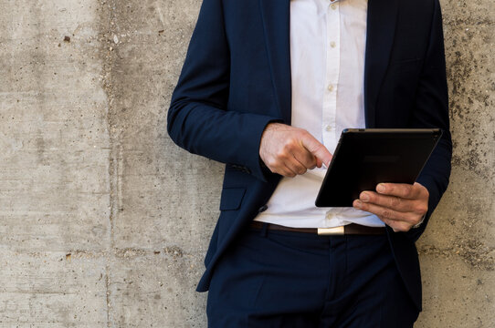 Midsection of a Businessman in a Navy Suit and White Shirt Holding and Interacting with a Black Digital Tablet, Illustrating Mobile Business and Technology Use