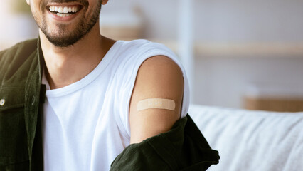 A young man smiles confidently while revealing a small bandage on his upper arm. The warm, sunny...