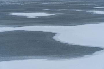 Melting of cold water and ice in river in early spring. Meltwater and white tones of ice contrast with the dark wave. Stream of snow in natural parkland. Global warming or climate change concept.