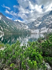 Serene view of a clear lake surrounded by towering mountains. Snow-capped peaks reflect in the calm water with lush greenery in the foreground. Perfect for nature lovers and photographers.