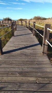 Strolling at sunset along a wooden boardwalk over the beach dunes. Time Lapse. Wooden walkways installed to protect the dunes and their flora and fauna, on Riumar beach in Catalonia, Spain. Vertical.