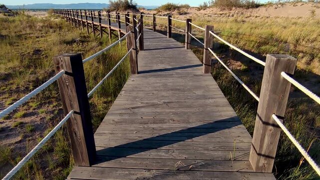 Strolling at sunset along a wooden boardwalk over the beach dunes. Time Lapse. Wooden walkways installed to protect the dunes and their flora and fauna, on Riumar beach in Catalonia, Spain.
