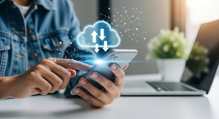 A person using a smartphone to access cloud storage, showcasing a modern digital workspace with a laptop and green plant.