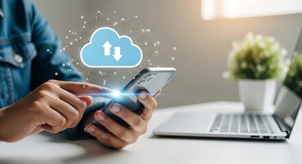 A close-up of a person using a smartphone to access cloud storage, with a laptop and decorative plant in the background.