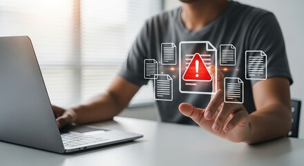 A young South Asian man interacting with digital warning icons, indicating a notification while using a laptop at a modern workspace.