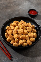 Golden crispy chicken popcorn with ketchup on a gray background. Fast food and snack concept.