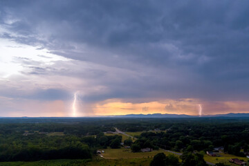Lightning strikes illuminate sky above serene valley during thunderstorm as sun sets