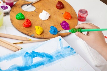 Child drawing art with brush, watercolor paints on desk