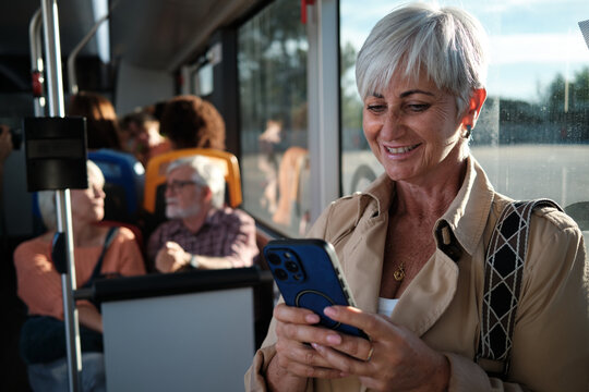 Senior woman smiling using smartphone on urban bus