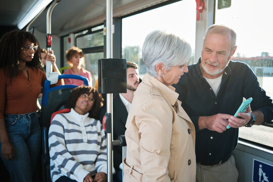 Senior man showing smartphone to woman on bus