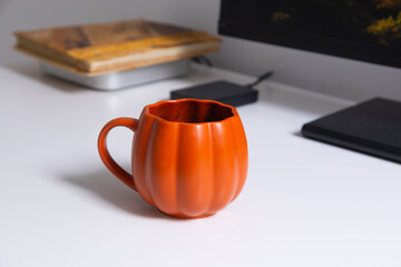 Orange mug on modern desk near monitor. Warmth, color accent, and daily comfort in creative workspace.