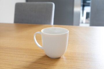 White ceramic mug on wooden table. Simplicity, calm, and balance of morning home routine. Copy space