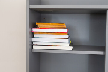 Stack of colorful books on gray shelf. Knowledge, organization, and creative inspiration in minimalist home interior.