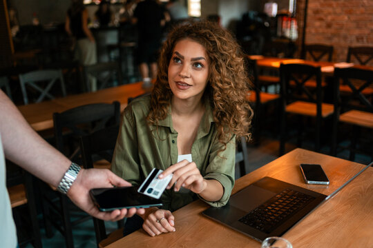 Woman paying with card at a cafe during a casual meeting in the evening - Powered by Adobe