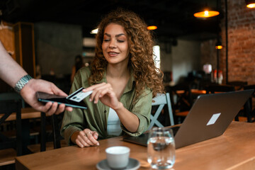 Young woman using smartphone at cafe during afternoon meeting with laptop on table
