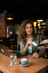 Woman paying for coffee while working on laptop in a cozy cafe setting