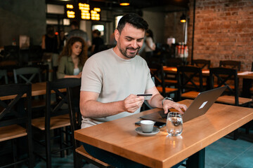 Man making an online purchase in a cozy cafe setting with a laptop and coffee