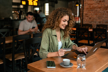 Young woman working on laptop in cozy cafe while making online purchase