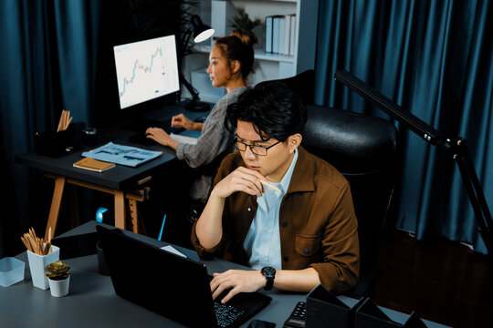 Businessman with stressful face looking on document file deadline while coworker trading stock exchange investment at late night time at modern office working on startup company project job. Infobahn.