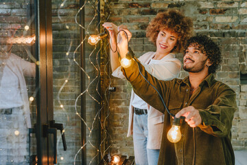 Young man and woman hanging garland standing near window indoor