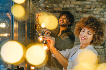Young man and woman hanging garland standing near window indoor