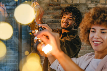 Young man and woman hanging garland standing near window indoor