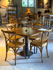 Empty cafe interior with wooden tables and chairs in soft daylight. Calm atmosphere, hospitality, and anticipation of social interaction.