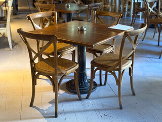 Wooden cafe table with chairs in sunlight near window. Quiet ambiance, balance of design and everyday rhythm of hospitality.