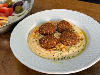 Plate of falafel served on creamy hummus with olive oil and herbs. Mediterranean cuisine, flavor, and aesthetic of healthy homemade food.