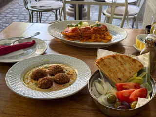 Mediterranean lunch table with falafel, pasta, pita bread, and fresh vegetables. Colorful meal, freshness, and balance of flavor in casual dining atmosphere.