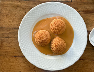 Three caramel cream puffs on white plate seen from above. Symmetry, texture, and sweetness creating elegant simplicity of dessert presentation.