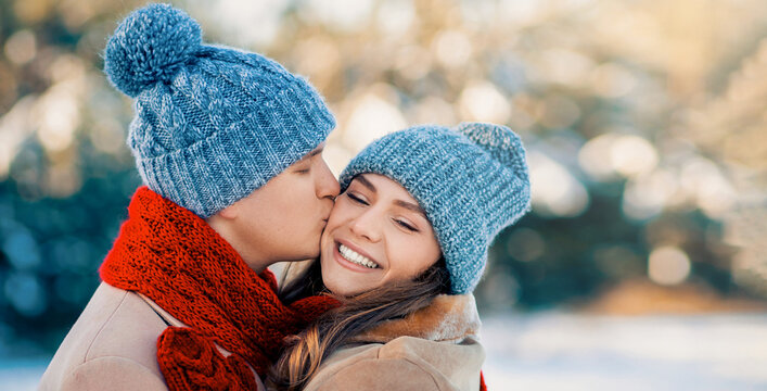 Young couple enjoys a joyful moment together in a winter setting. They are bundled in warm clothes, smiling, while surrounded by snow-covered trees basking in the sunlight. - Powered by Adobe