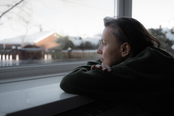 Thoughtful sad woman sitting on a windowsill. Mental health and seasonal disorder. Winter scenery...