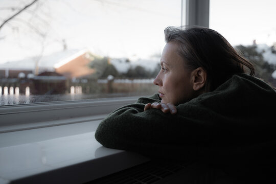 Thoughtful sad woman sitting on a windowsill. Mental health and seasonal disorder. Winter scenery outside