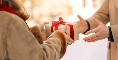 A person hands a wrapped gift adorned with a red bow to another individual, creating a moment of...