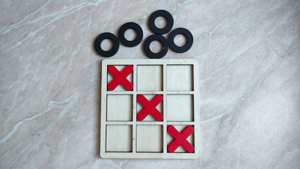 Tic tac toe game on marble surface with red x and black o pieces.
