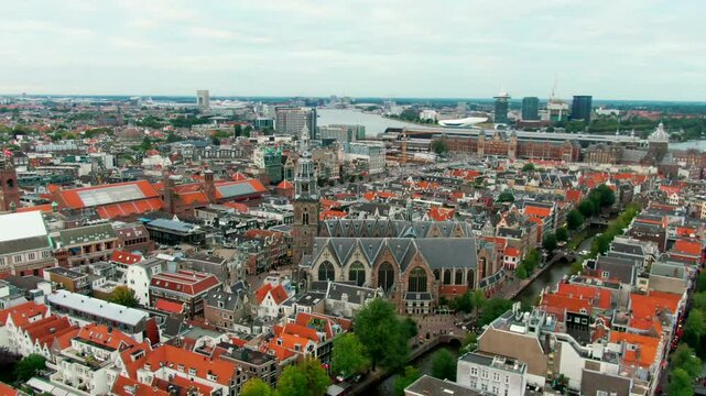 Drone shot over Amsterdam city center with Oude Kerk, traditional Dutch architecture, red roofs, and canal layout. Perfect for travel, tourism, and urban heritage content. 4K establishing aerial view