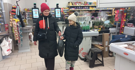 A woman and a girl leave a grocery store together in winter.