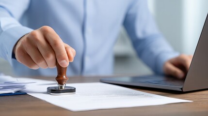 Confident professional stamping important document with approval seal, signifying official confirmation and business process efficiency on desk beside laptop.