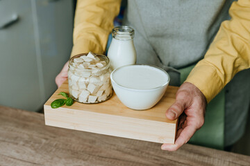 Close up of male hands holding wooden tray with tofu, yogurt and milk