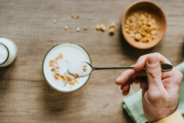 Top view of man adding granola to yogurt bowl on wooden background