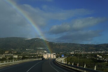 Naklejka premium A rainbow through a wet car windshield. Road trips. An atmospheric and dynamic landscape capturing the contrast between rain and sun.