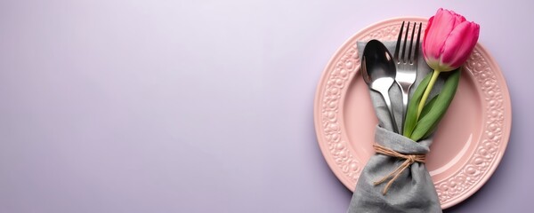 Pink plate setting with gray napkin cutlery and vibrant tulip flower. Simple elegant table arrangement for spring event or celebratory meal. Soft lilac backdrop adds fresh clean feel.