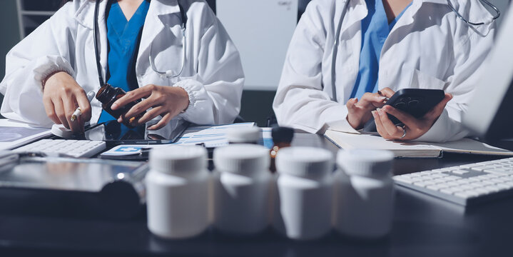 Two doctors and a female nurse meet at a table in the hospital, collaborating on medical tasks using laptops and computers