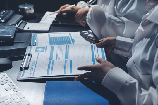 Two doctors and a female nurse meet at a table in the hospital, collaborating on medical tasks using laptops and computers - Powered by Adobe