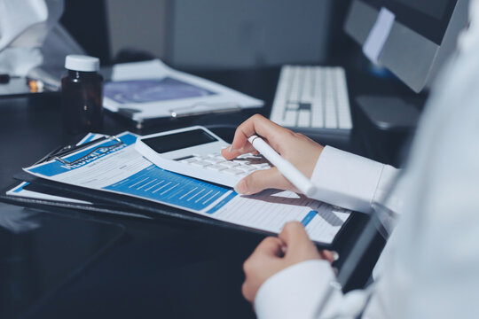 Two doctors and a female nurse meet at a table in the hospital, collaborating on medical tasks using laptops and computers
