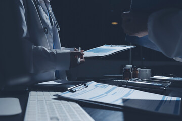 Two doctors and a female nurse meet at a table in the hospital, collaborating on medical tasks using laptops and computers